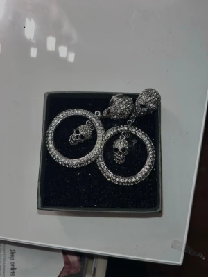Glittriga döskalleörhängen Rock by Sweden - Säljer ett par riktigt coola örhängen från Rock by Sweden av Laila Bagge. De är stora, runda hoops i silverfärg med massor av gnistrande stenar och detaljerade döskallar både upptill och hängande i mitten. Perfekta för dig som vill sticka ut och addera lite edge till din stil. Nypris 799kr