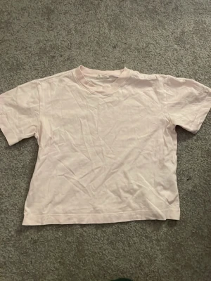 Ljusrosa basic t-shirt Gina Tricot - En enkel och clean ljusrosa t-shirt från Gina Tricot, basically basics-kollektionen. Klassisk rund halsringning och korta ärmar. Perfekt till jeans eller shorts för en chill look.