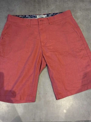 Rosa linneshorts från Dressmann - Säljer ett par snygga rosa shorts från Dressmann i linnemix. Klassisk modell med normal passform, bälteshällor, sidofickor och bakfickor med knapp. Stängs med dragkedja och knapp framtill. Perfekta för varma dagar.