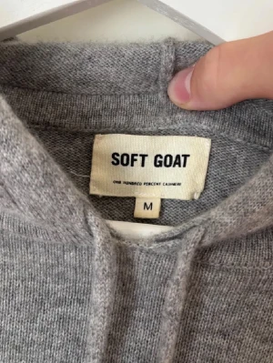 Grå hoodie i kashmir från Soft Goat - Mjuk och stilren grå hoodie från Soft Goat i 100% kashmir. Tröjan har huva med snörning, ribbade muddar och lång ärm. Perfekt för dig som vill ha en lyxig och bekväm vardagslook med en clean vibe.