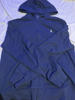 Mörkblå polo ralph lauren hoodie - Säljer nu en mörkblå polo ralph lauren hoodie med vitt tryck. Helt oanvänd pga lite för stor, den är lite mindre i storleken igentligen är det storlek L men passar också väldigt bra till storlek S. Skriv om ni har fler frågor!