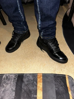 Svarta Nike sneakers med fuskpäls - Säljer ett par svarta Nike sneakers i high modell med snörning och rund tå. Skorna är i skinn och har mjuk grå fuskpäls på insidan för extra värme. Klassisk Nike-logga på sidan och svart sula. Perfekta för dig som vill ha både stil och komfort.