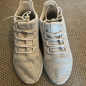 Ljusgrå Adidas sneakers i mesh - Säljer ett par ljusgrå Adidas sneakers med stickad mesh-överdel och vita detaljer. Skorna har rund tå, snörning och en mjuk, platt sula. Perfekta för dig som gillar en clean och sportig look. Adidas-logga på plös och häl.