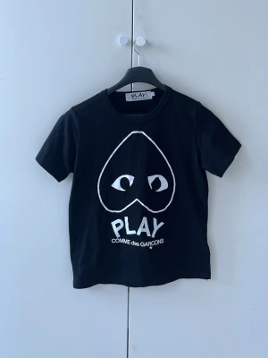 Svart Comme des Garçons PLAY t-shirt - Svart t-shirt från Comme des Garçons PLAY med ikoniskt hjärta med ögon tryckt i vitt på bröstet. Klassisk rund hals och korta ärmar. Skriv vid frågor eller funderingar 🙂