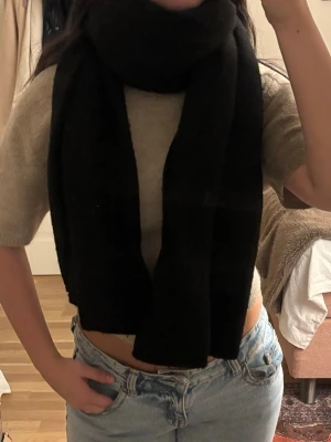 Svart stickad halsduk  - Säljer en svart stickad halsduk från Zara i storlek M. Halsduken har en rak och croppad passform och är gjord i ett mjukt stickat material.