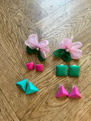 Färgglada retro örhängen i plast - Säljer ett set med fem par örhängen i olika former och färger. Två par trekantiga i turkos och rosa, två par fyrkantiga i rosa och grönt samt ett par stora blommor i rosa och grönt med pärldetalj. Alla är i plast och har cool retrostil.