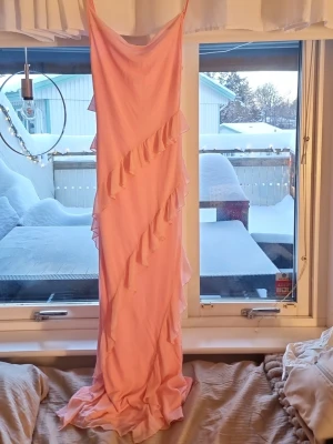Ljusrosa långklänning med volanger - Säljer en superfin ljusrosa långklänning med tunna axelband och diagonala volangdetaljer framtill. 