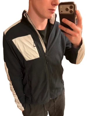  Fleece från Helly Hansen - Säljer en mörkblå fleece från Helly Hansen med vita detaljer på axlar, ärmar och bröstficka. Jackan har dragkedja framtill, hög krage och två sidofickor med dragkedja. Loggan på bröstet har tyvärr fallit av. Annars mycket fint skick. 