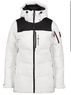 Vit och svart dunjacka Sail Racing - Säljer en snygg vit dunjacka från Sail Racing med svarta detaljer över axlar och huva. Jackan har dragkedja framtill, huva och flera praktiska fickor. Perfekt för kalla dagar och riktigt stilren look.