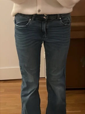 Blå bootcut jeans med snygga fickor - Säljer ett par blå jeans med bootcut passform och snygga fickor bak med knappar. Jeansen har klassisk femficksdesign fram och är i ett mjukt denimtyg. Snygg tvättad look och medium midja.  Dem är köpta från Ullared och är använda och lite slitna längst ner storlek 164. Lätta att styla. Pris går att diskuteras!