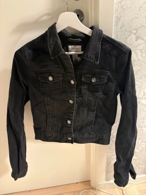 Svart jeansjacka från Forever 21 - Snygg svart jeansjacka från Forever 21 i storlek M.  Men skulle säga att den mer passar någon som har storlek S/XS. Klassisk modell med krage, silverfärgade knappar och två bröstfickor med lock. Jackan har lång ärm och är lätt croppad för en trendig look. Perfekt att slänga över en hoodie eller t-shirt.