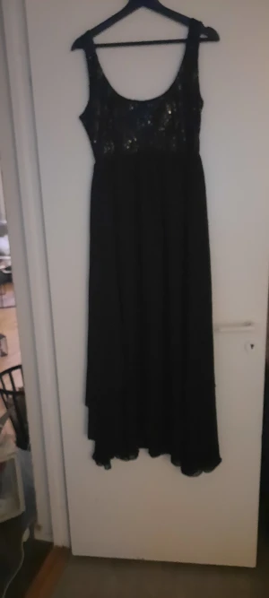 Svart långklänning med paljetter,vacker jul o nyårs klänning. - Svart långklänning från Paris Kate & I i storlek 38. Överdelen är täckt med glittriga paljetter som ger en snygg och festlig look, medan kjolen är enkel och faller mjukt. Klänningen är ärmlös och har rundad urringning. Perfekt för dig som vill sticka ut.