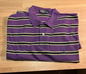 Randig lila Polo Ralph Lauren skjorta XL - Snygg lila skjorta från Polo Ralph Lauren i storlek XL med klassiska gula och svarta ränder. Skjortan har krage, knappar framtill och den ikoniska broderade Polo-loggan på bröstet. Tillverkad i 100% bomull för skön känsla och stil.
