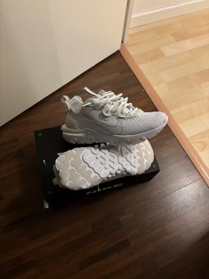 Nike React sneakers helvita - Nike React sneakers i helvit färg med snyggt mönstrad sula och ventilerande mesh-överdel. Skorna har snörning och en chunky, vågig plattformsula som ger grym komfort och stil. Perfekta för dig som gillar cleana och sportiga sneakers med modern vibe. Helt oanvända aldrig testat då jag har 2 par