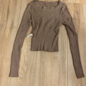 Brun ribbad långärmad topp - Snygg brun långärmad topp med ribbad struktur och rund hals. Modellen är figurnära och har en något croppad passform. Perfekt att styla med jeans eller kjol för en trendig look.