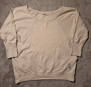 Beige loose sweatshirt med broderi House of Lola - Snygg beige sweatshirt från House of Lola. Loose passform och trekvartsärm. Tröjan har ett diskret broderat blommotiv vid nederkanten och breda muddar vid ärmslut. Perfekt för dig som gillar enkel stil med en liten detalj.