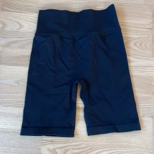 Svarta biker shorts från New Apparel - Svarta biker shorts från New Apparel i storlek S. De har hög midja och är tillverkade i ett ribbat, stretchigt syntetmaterial som sitter skönt och följer kroppen. Perfekta för träning eller chill. Enkla att matcha med hoodies eller crop tops. Aldrig använda!
