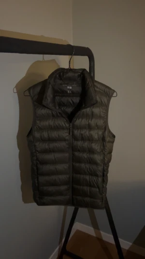 Grön väst - Säljer en mörkgrön, ultralätt dunväst från Uniqlo i storlek XS. Västen har en clean, quiltad design med ståkrage och dragkedja framtill. Materialet är syntet med dunfyllning, perfekt för lager-på-lager och chill stil. 