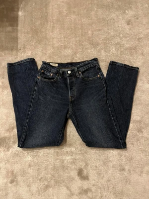 Levi's 501 mörkblå jeans straight fit - Säljer ett par helt nya  klassiska Levi's 501 jeans i mörkblå tvätt med raka ben och normal passform. Jeansen har fem fickor, knappgylf och snygga kontrastsömmar. Perfekt för dig som gillar tidlös stil och vill ha ett par jeans som funkar till allt. W25 L30. Modellen på bilden är 177 cm och 60 kg för referens. Hör gärna av dig vid frågor eller funderingar. Pris kan alltid diskuteras 😁.