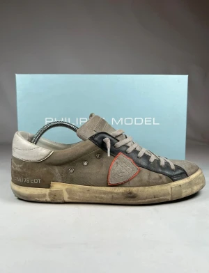 Philippe Model grå stl 43 - Snygga sneakers från Philippe Model i storlek 43 i grå och svart mocka med vita detaljer och snörning. Skorna har en rund tå, platt sula och en ikonisk sköld på sidan med röd kant. Perfekt för dig som gillar en cool och avslappnad stil. Hör gärna av dig vid frågor och funderingar. Pris kan alltid diskuteras. 