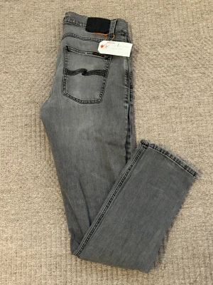 Nudie Jeans - Vi säljer nu ett par snygga gråa jeans från Nudie Jeans med klassisk femficksdesign och svarta detaljer på bakfickan. Modellen  har en smal-medium passform och raka ben. Jeansen är tillverkade i mjukt denimtyg med lätt tvättad look och har normal midja. Vi säljer dessa till ett kanonpris. Observera att jeansen har blivit lagade på Nudie Jeans butik i Göteborg och är nu som nya, i toppskick. Tveka inte på att höra av dig vid minsta lilla fråga! Priset kan diskuteras vid snabb och smidig affär. 😁😁