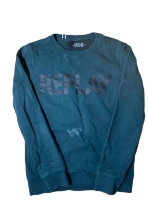 Mörkgrön sweatshirt från Replay - En mörkgrön sweatshirt från Replay med tryckt logga framtill. Tröjan har rund halsringning och långa ärmar. Tillverkad i mjuk bomull, perfekt för chill dagar. Klassisk passform och stilren look.