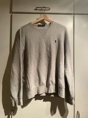 Grå sweatshirt från Polo Ralph Lauren - Snygg grå sweatshirt från Polo Ralph Lauren med klassisk rund hals och broderad marinblå logga på bröstet. Inga defekter och passar loose.