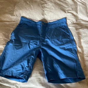 Blå och röda bomullsshorts från Race Marine - Två par klassiska shorts från Race Marine, ett par i klarblått och ett par i rött. Båda har normal passform, sidofickor, bakfickor med knapp och bälteshällor. Tillverkade i mjuk bomull, perfekta för varma dagar. Snygg, enkel design som funkar till det mesta.