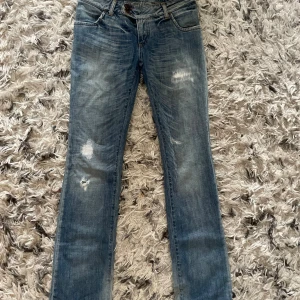 Blå slitna jeans  - Snygga blå bootcut jeans med slitningar. Jeansen har klassisk femficksdesign, dubbla knappar i midjan och coola slitdetaljer framtill. Perfekt för en avslappnad och trendig look.