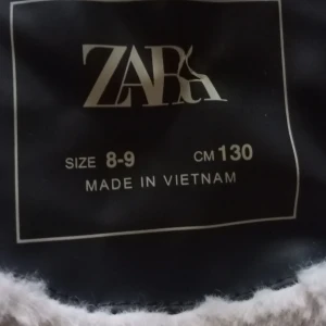 Svart teddyfodrad jacka från Zara - Cool svart jacka från Zara med mjukt teddyfoder i beige. Jackan har huva, stora fickor framtill och stängs med knappar. Utsidan är i syntetmaterial som ger en skinnlook, perfekt för kalla dagar när du vill vara både varm och snygg.