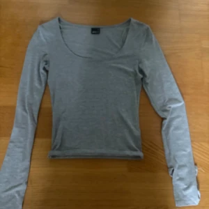 Grå långärmad topp Gina Tricot XS - En enkel och stilren grå långärmad topp från Gina Tricot i storlek XS. Toppen har rundad halsringning och är figurnära i modellen. Perfekt att matcha med jeans eller kjol för en clean look.