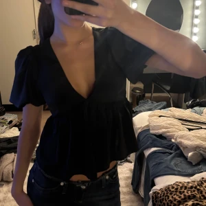 Svart blus med puffärm och v-ringning - Supersnygg svart blus från nelly med djup v-ringning och puffiga korta ärmar. Modellen är croppad med volang nedtill.