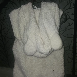 Vit teddyväst med huva från F&F - Mysig vit teddyväst från F&F med huva och dragkedja framtill. Västen har två fickor och är gjord i fluffigt fleece-material som ger en cool och avslappnad look. Perfekt för lager-på-lager-stil under kyliga dagar.