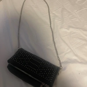 Svart axelväska med nitar och kedja - Säljer min väska som jag inte använt på länge. Använd kanske 5 gånger men inga tecken på användning. Super fin och bra att ha om man vill ha en liten men fortfarande rymlig väska. 