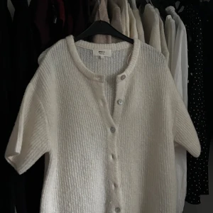 Vit stickad kofta från Gina Tricot - Säljer en vit stickad kofta från Gina Tricot med korta ärmar och rund hals. Koftan har ribbad struktur och knappar framtill som ger en chill och enkel look. Perfekt att slänga på över en topp för extra lager. storlek S