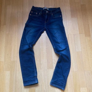 Levi's 511 blå jeans - Säljer ett par klassiska Levi's 511 jeans i mörkblå denim. Modellen har smal passform med raka ben och fem fickor. Typisk Levi's-detalj med röd etikett på bakfickan. Perfekta för dig som gillar en clean och tidlös look.