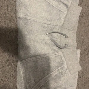 Grå mjukisbyxor Juicy Couture XXS - Supermysiga grå mjukisbyxor från Juicy Couture i storlek XXS. Byxorna har snörning i midjan, stora fickor fram och bakficka med knappdetalj. Perfekta för chill dagar och har den klassiska Juicy-looken.