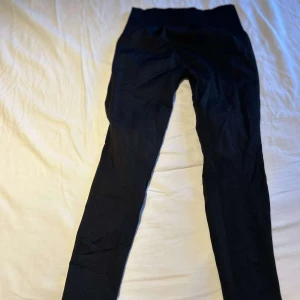 Svarta leggings från ICANIWILL - Snygga svarta leggings från ICANIWILL med hög midja och diskret logga på höften. De är tighta och stretchiga, perfekta för gymmet eller löprundan. Materialet är mjukt och följsamt, vilket ger en skön passform och rörelsefrihet.