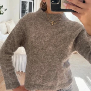 Brun stickad tröja med hög krage - Mysig beige stickad tröja med hög krage och långa ärmar. Tröjan har en rak passform och ribbade muddar vid hals, ärmslut och nederkant. Perfekt för lager-på-lager och chill dagar.