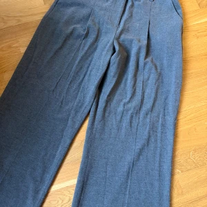 Grå kostymbyxor från BikBok - Stilrena grå kostymbyxor från BikBok i storlek 46. Byxorna har hög midja, vida ben och pressveck framtill. Tillverkade i ett mjukt material med bälteshällor och diskreta fickor. Perfekta för en clean och dressad look.