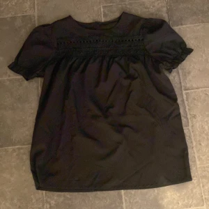 Svart blus med spetsdetaljer - Säljer en svart blus med korta puffärmar och fina spetsdetaljer. 