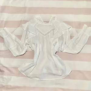 Vit  blus med spetsdetaljer från ONLY - Supersöt vit blus med volangdetaljer och breda långa ärmar. Blusen har v-ringning med spets och dekorativa sömmar, samt rynkade partier och romantisk känsla. Perfekt för dig som gillar vintagevibbar och feminina detaljer. Lappen är inte kvar men den är från ONLY och skulle gissa på att den är i storlek XS-XSS.Priset kan sänkas!💕