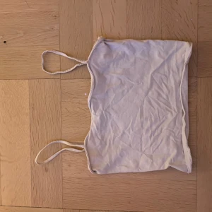 Vit bandeau tubtopp med smala axelband - En enkel vit bandeau tubtopp med smala axelband. Toppen är ärmlös och har en rak, croppad passform. Perfekt för varma dagar eller som lager under andra plagg. Materialet känns mjukt och stretchigt.