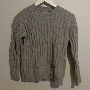 Grå stickad tröja från SHEIN - Mysig grå stickad tröja från SHEIN i storlek M. Tröjan har ett snyggt kabelstickat mönster, rund halsringning och ribbade muddar vid ärmslut och nederkant. Perfekt för kyliga dagar när du vill vara både varm och stilren.