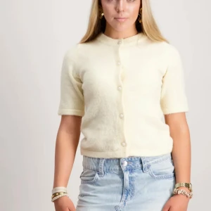 Ljusgul kofta med pärlknappar - Söt ljusgul kofta med korta ärmar och pärlknappar framtill. Koftan är stickad och har en mjuk, fluffig känsla. Perfekt att slänga över en topp eller klänning för en chill och stilren look.
