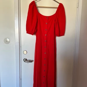 Röd långklänning med puffärm från H&M - Superfin röd långklänning från H&M i 100% bomull med puffiga korta ärmar, knappar hela vägen framtill och ett knytband i midjan. Stl 34, passar xs/s. Använd 1 gång. 