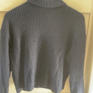 Svart ribbad polotröja - Mysig svart polotröja med ribbad struktur och lång ärm. Perfekt för kyliga dagar och enkel att matcha med olika outfits. Hög krage och avslappnad passform ger en skön och stilren look.