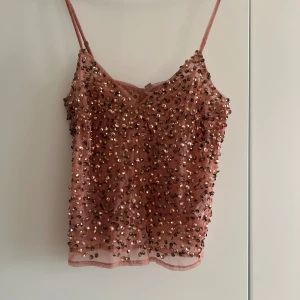 Rosa paljettopp från ASOS - Supersnygg rosa linnetopp från ASOS med tunna axelband och täckt av glittriga paljetter. Toppen har en lätt transparent meshbas och är perfekt för att sticka ut. Den är croppad och har en feminin v-ringning framtill.