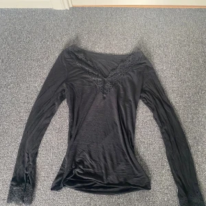 Svart långärmad topp med spets från Intimissimi - Svart långärmad topp från Intimissimi med v-ringning och fina spetsdetaljer vid halsringning och ärmslut. Tunn och mjuk kvalitet med inslag av kashmir, perfekt för lager-på-lager eller som en snygg detalj till outfiten.