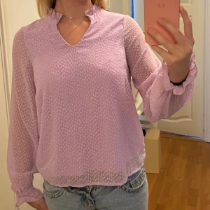 Ljuslila blus med strukturmönster - Supersöt ljuslila blus med diskret strukturmönster och lätt transparenta ärmar. Blusen har v-ringning med liten volangkant vid halsen och långa ärmar med resår och volang vid ärmslut🫶🏻 storlek Xs